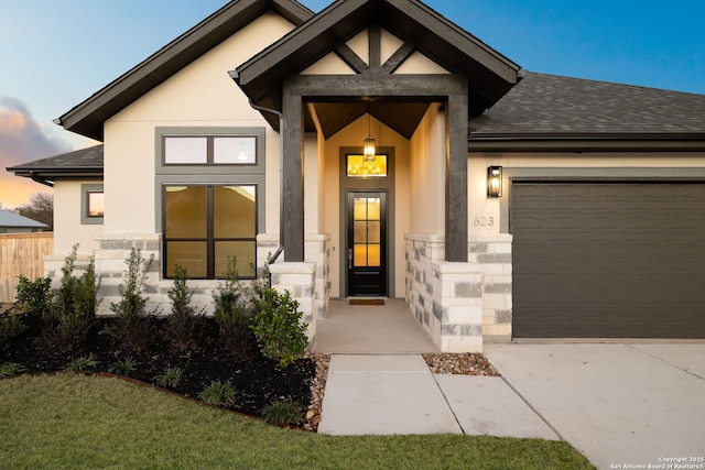 view of exterior entry with a garage, roof with shingles, and stucco siding