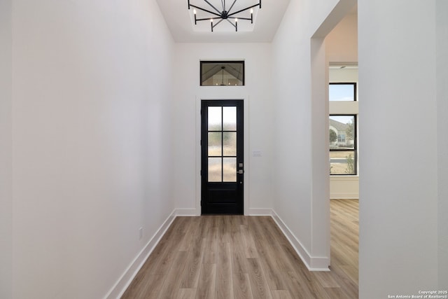 foyer entrance featuring light wood-type flooring, a wealth of natural light, baseboards, and an inviting chandelier