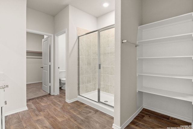 bathroom with baseboards, toilet, wood finished floors, a walk in closet, and a shower stall