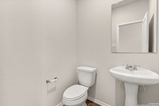 half bath featuring wood finished floors, toilet, and baseboards