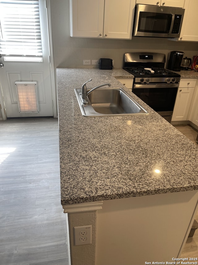 kitchen featuring appliances with stainless steel finishes, dark stone countertops, a sink, and white cabinets