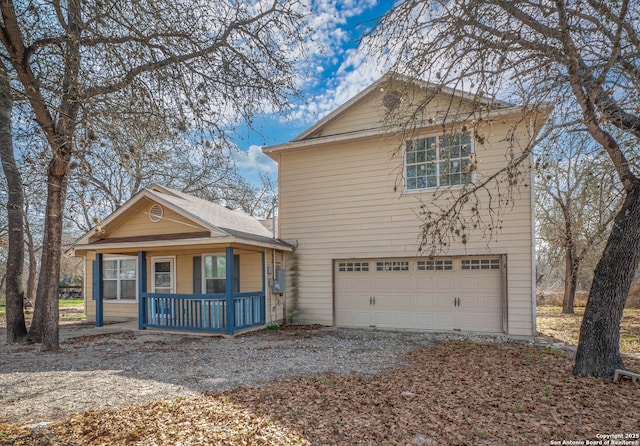 traditional-style house with covered porch, gravel driveway, and a garage