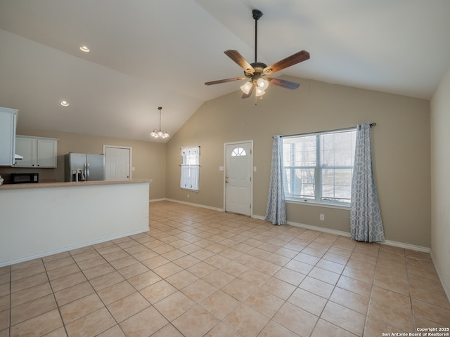 interior space featuring lofted ceiling, light tile patterned flooring, baseboards, and ceiling fan with notable chandelier