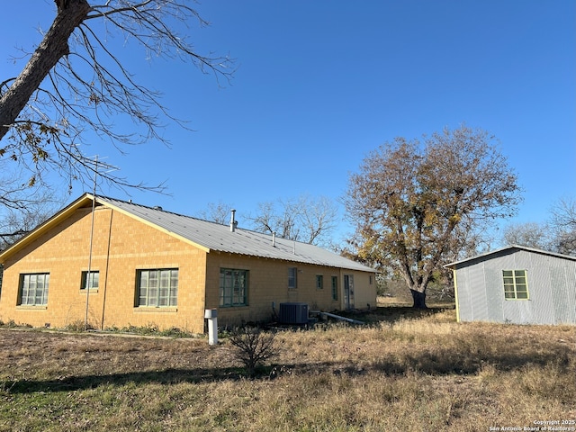 rear view of property with an outbuilding, metal roof, and central AC unit