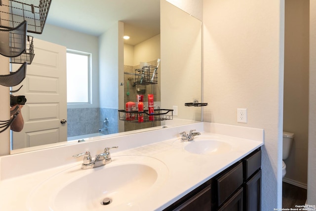 full bath featuring tiled shower, a sink, toilet, and double vanity