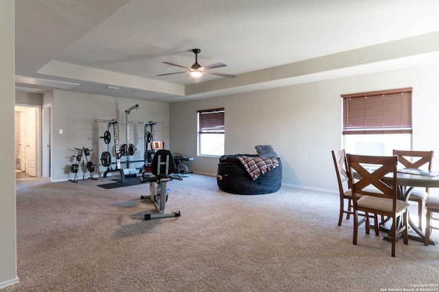 workout area with carpet floors, ceiling fan, a tray ceiling, and baseboards