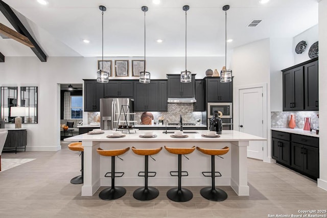 kitchen featuring under cabinet range hood, stainless steel appliances, visible vents, a kitchen breakfast bar, and light countertops