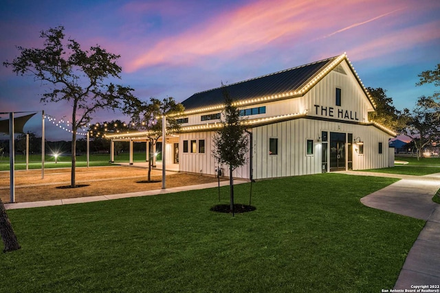 back of house at dusk featuring metal roof, a yard, and board and batten siding