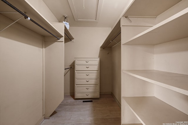 spacious closet with light wood finished floors and attic access