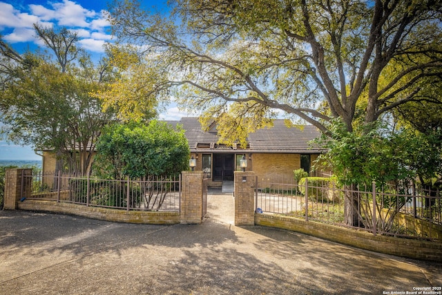 view of front facade with a tiled roof, brick siding, a fenced front yard, and a gate