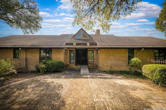 view of front of property with a tiled roof, brick siding, and a chimney