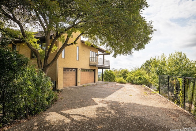 view of side of property with a garage, driveway, fence, and stucco siding