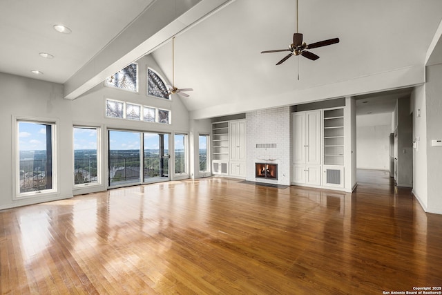 unfurnished living room with high vaulted ceiling, built in shelves, hardwood / wood-style flooring, a ceiling fan, and a brick fireplace