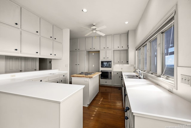 kitchen with black microwave, wall oven, a sink, a center island, and dark wood-style floors