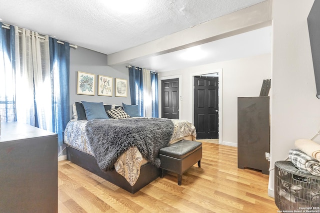 bedroom with a textured ceiling, light wood finished floors, beamed ceiling, and baseboards