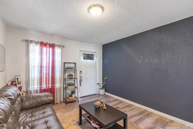 living area featuring a textured wall, light wood-style flooring, baseboards, and a textured ceiling