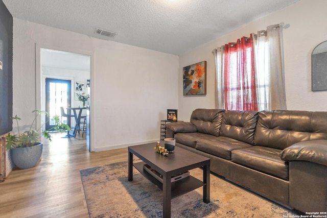 living area with plenty of natural light, a textured ceiling, visible vents, and wood finished floors