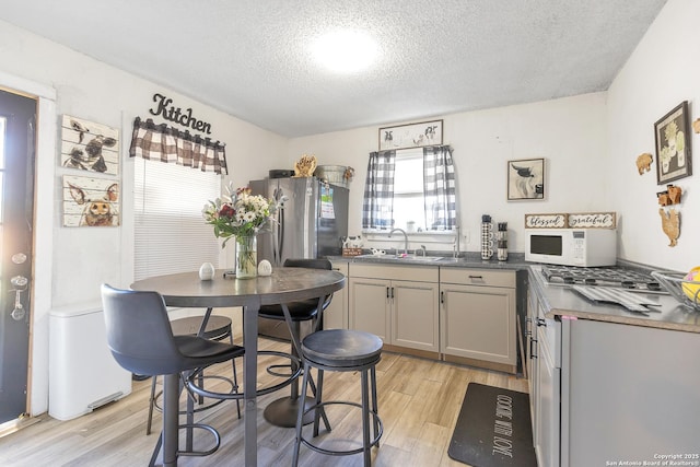 kitchen with light wood finished floors, dark countertops, white microwave, a sink, and a textured ceiling