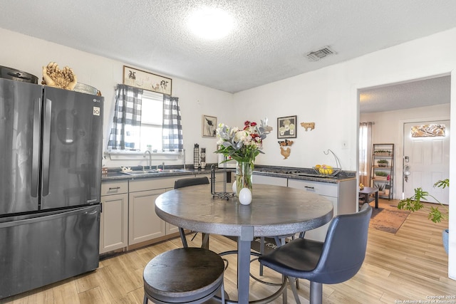 kitchen featuring light wood-style flooring, a sink, visible vents, freestanding refrigerator, and dark countertops