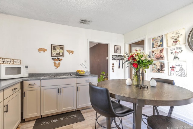 dining space with light wood-style floors, visible vents, and a textured ceiling