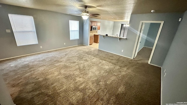 interior space with a ceiling fan, light colored carpet, a textured ceiling, and baseboards