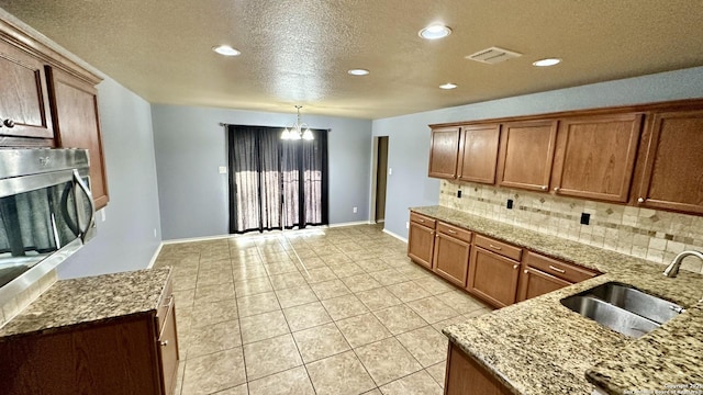 915 Ridingate Farm, San Antonio, TX 78228 - kitchen featuring visible vents, brown cabinetry, decorative backsplash, light stone counters, and a sink