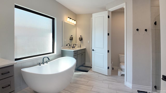 bathroom with a freestanding tub, baseboards, vanity, and toilet