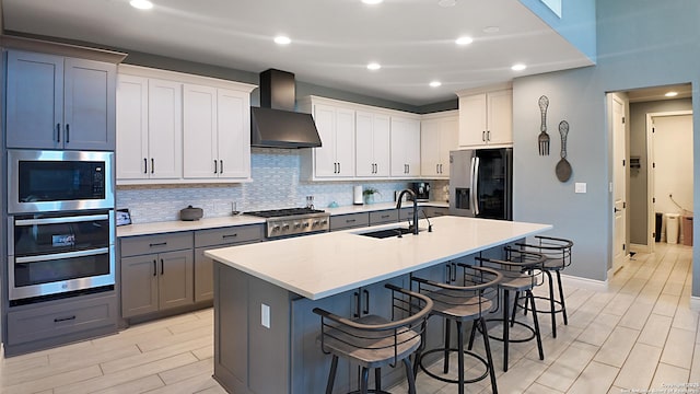 kitchen featuring a breakfast bar, tasteful backsplash, appliances with stainless steel finishes, a sink, and wall chimney range hood