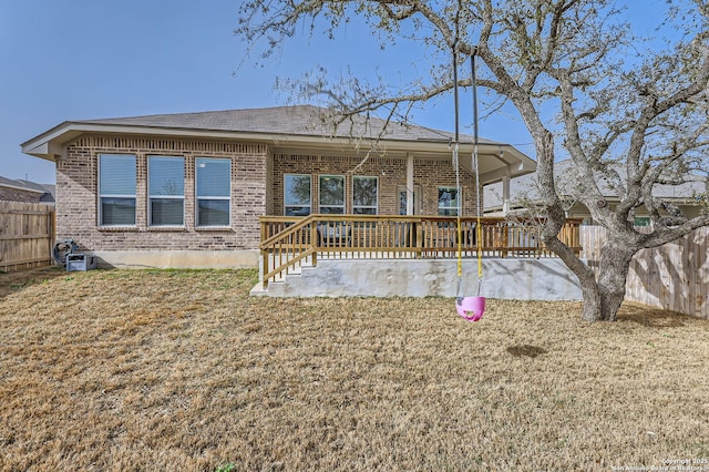 back of house with brick siding, a lawn, and fence