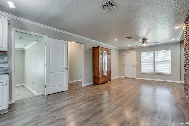 unfurnished living room featuring a textured ceiling, ornamental molding, light wood-type flooring, and visible vents