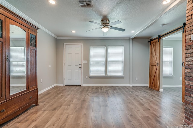 interior space with crown molding, visible vents, a barn door, light wood-style floors, and ceiling fan