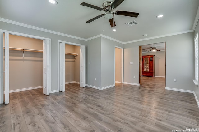 unfurnished bedroom with ornamental molding, light wood-style flooring, visible vents, and multiple closets