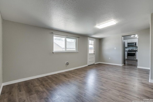 spare room featuring a textured ceiling, dark wood-type flooring, and baseboards