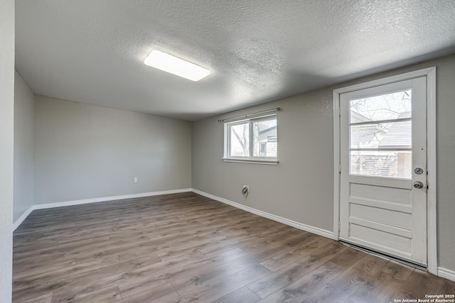 empty room featuring a textured ceiling, baseboards, and wood finished floors