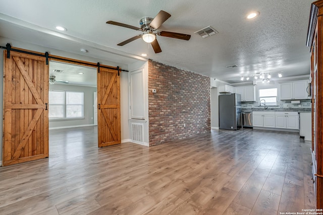 unfurnished living room with a barn door, visible vents, light wood-style flooring, and a textured ceiling