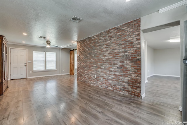 unfurnished living room with light wood-type flooring, visible vents, and brick wall