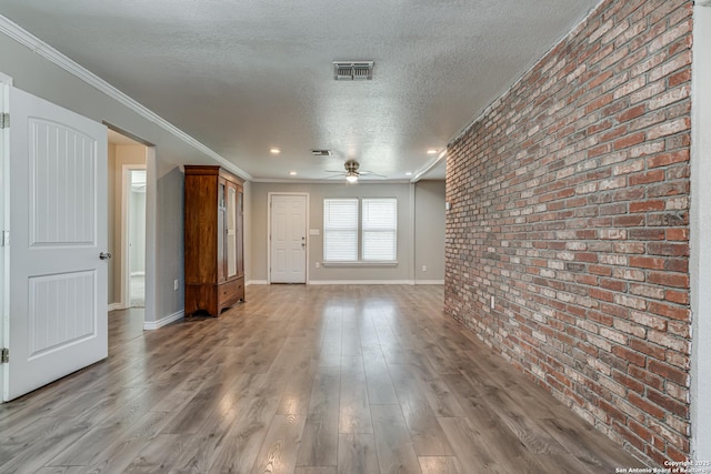 spare room featuring visible vents, light wood-style flooring, ceiling fan, a textured ceiling, and brick wall