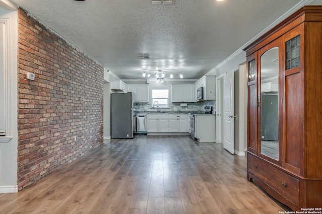 kitchen featuring light wood finished floors, decorative backsplash, appliances with stainless steel finishes, a textured ceiling, and brick wall