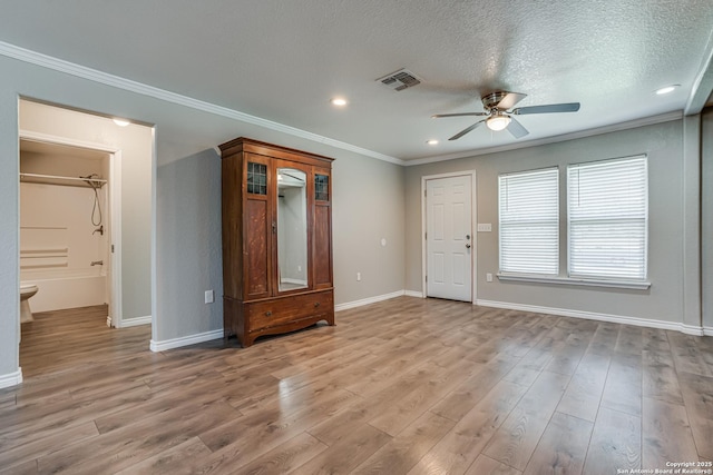 unfurnished room with light wood finished floors, baseboards, visible vents, ornamental molding, and a textured ceiling