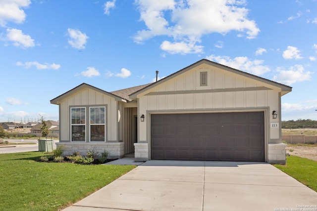 view of front of home featuring concrete driveway, stone siding, an attached garage, a front lawn, and board and batten siding