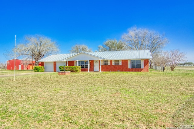 ranch-style home with an attached garage, metal roof, a front lawn, and brick siding