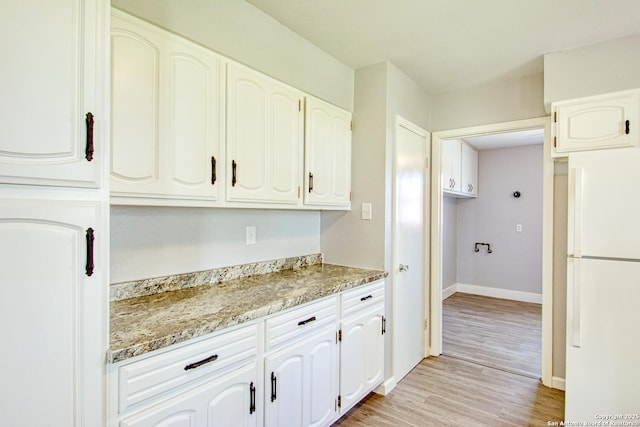 kitchen with light wood-type flooring, light stone countertops, white cabinetry, and freestanding refrigerator