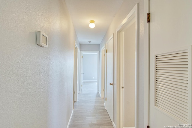 hallway featuring baseboards, a textured wall, and light wood finished floors