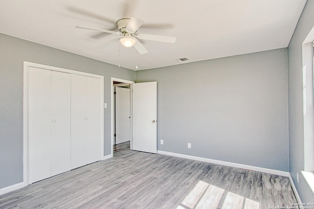 unfurnished bedroom featuring ceiling fan, visible vents, baseboards, light wood-style floors, and a closet