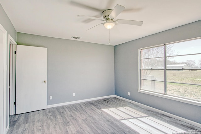 empty room with baseboards, wood finished floors, visible vents, and a healthy amount of sunlight