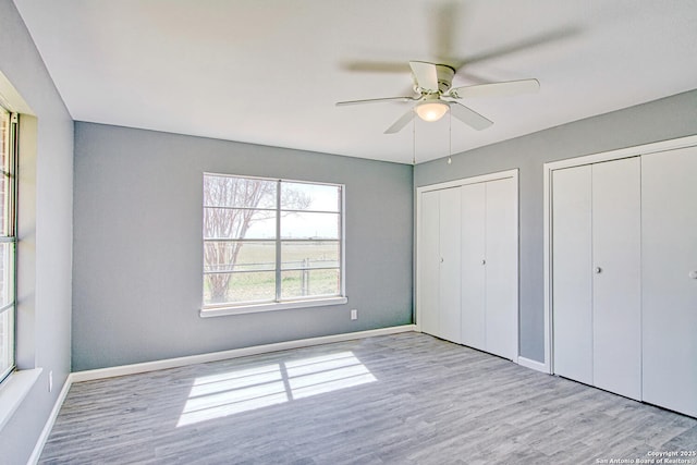 unfurnished bedroom with wood finished floors, baseboards, and two closets