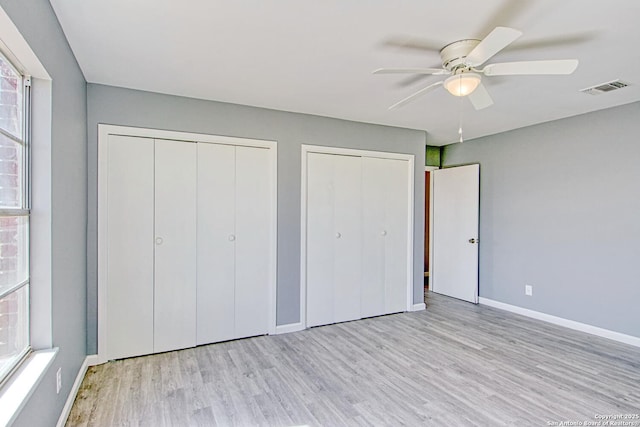 unfurnished bedroom featuring ceiling fan, wood finished floors, visible vents, baseboards, and multiple closets