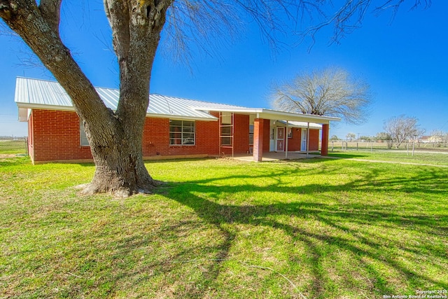 back of house featuring a yard, metal roof, and brick siding