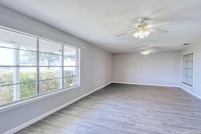 spare room with a ceiling fan, visible vents, baseboards, and wood finished floors