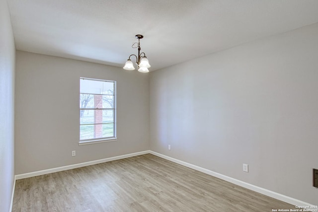 empty room with an inviting chandelier, baseboards, and wood finished floors